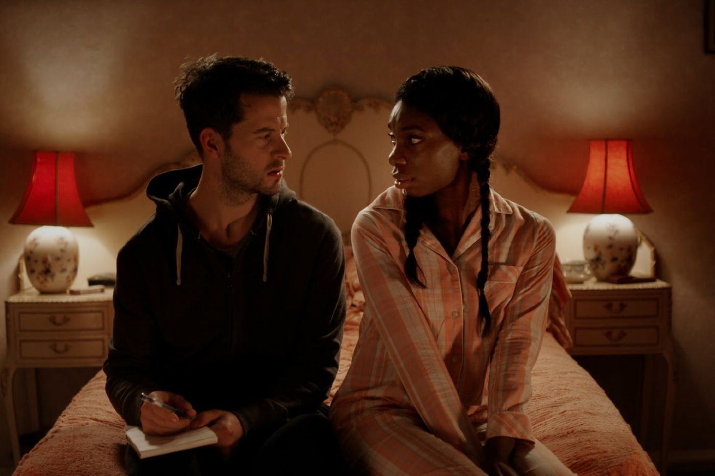 Connor y Tracey sentados al borde de la cama conversando.