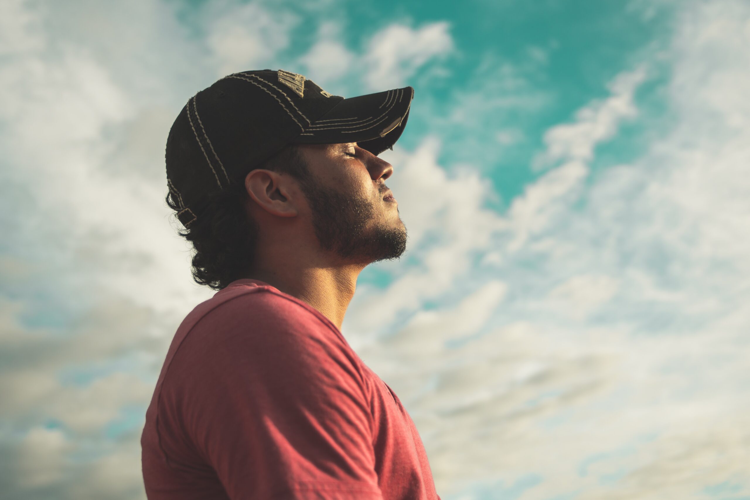 Un hombre con una gorra de b&eacute;isbol mira al cielo con los ojos cerrados y una sonrisa.