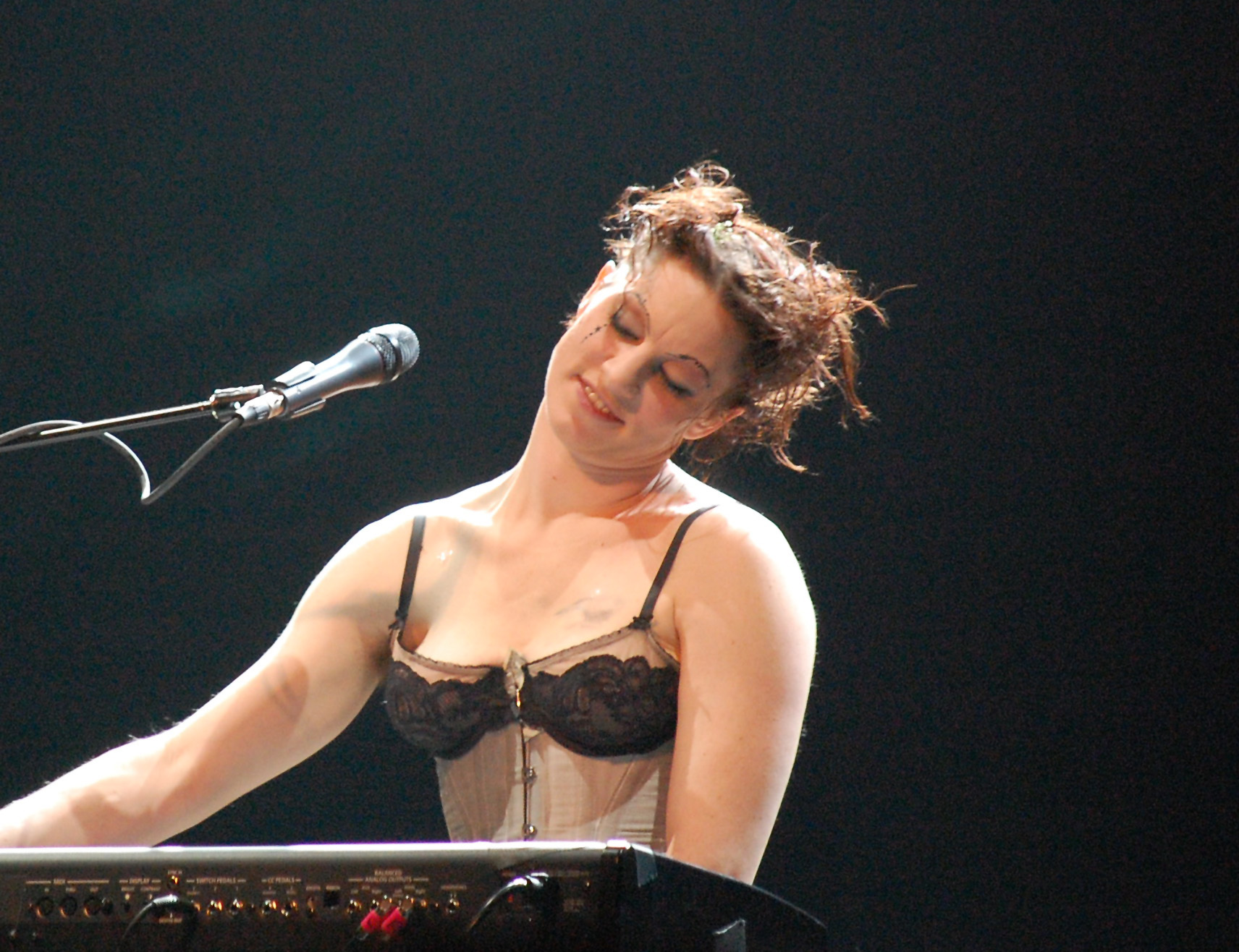 Amanda performing on sitting on the piano and tilting her head smiling with eyes closed.