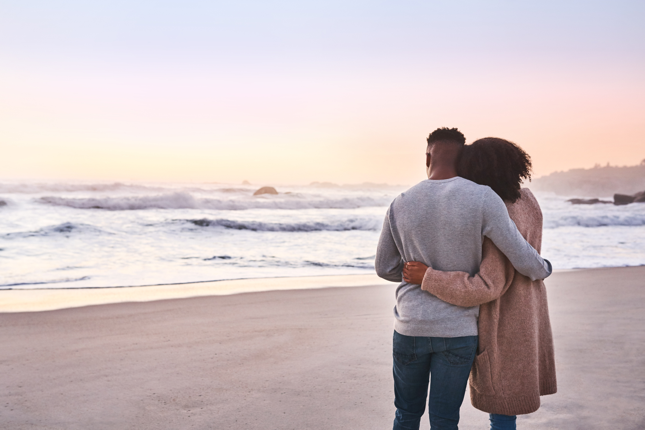 Una pareja negra comparte un momento &iacute;ntimo mirando el amanecer sobre la playa abrazados.