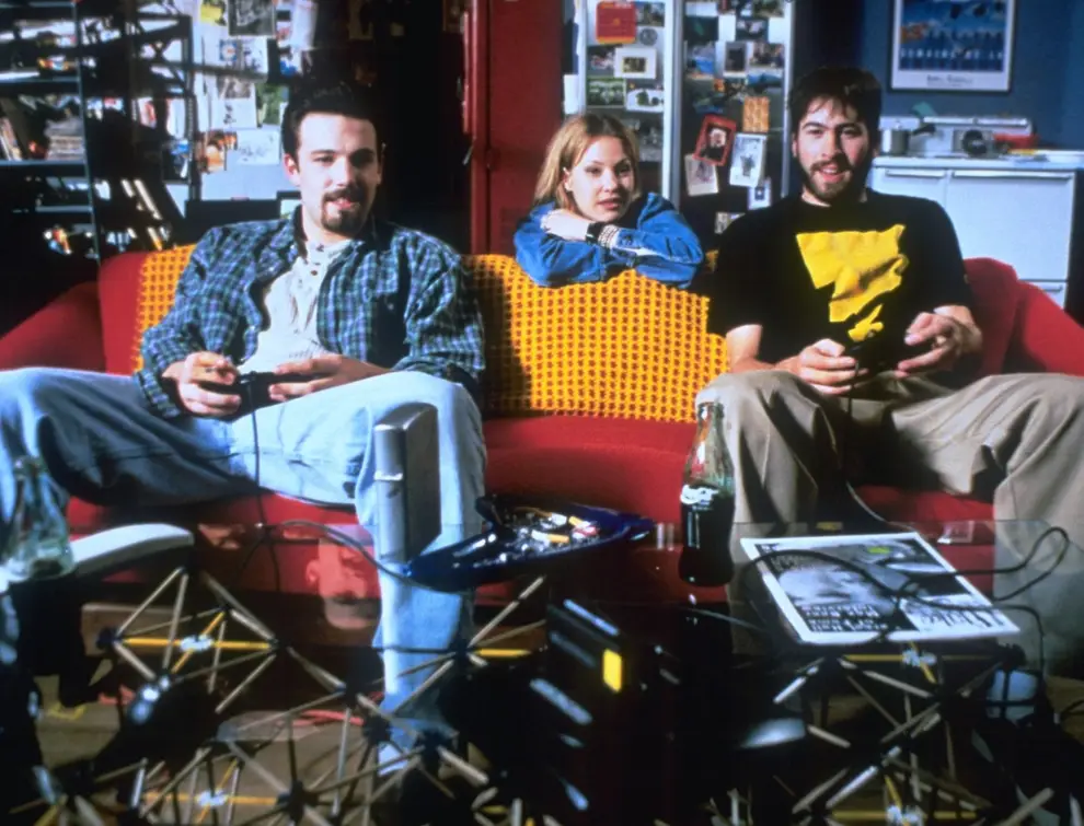 Holden Banken sit on the couch playing a videogame while Alyssa is sitting behind them watching them play.