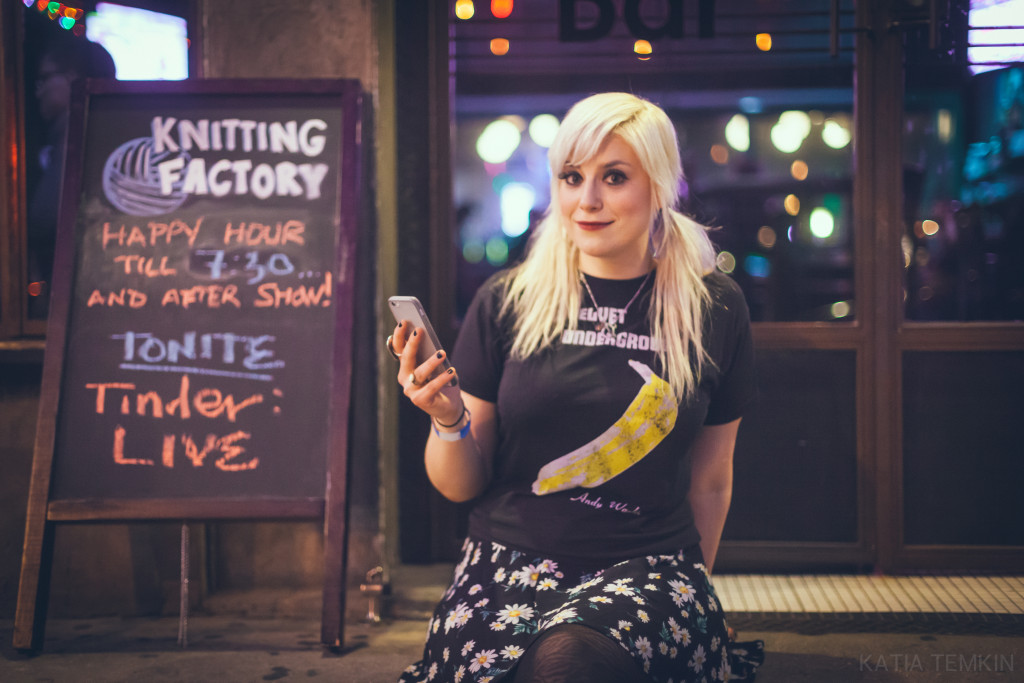 Lane Moore smiling holing her phone sitting outside the location of her even for tinder live.