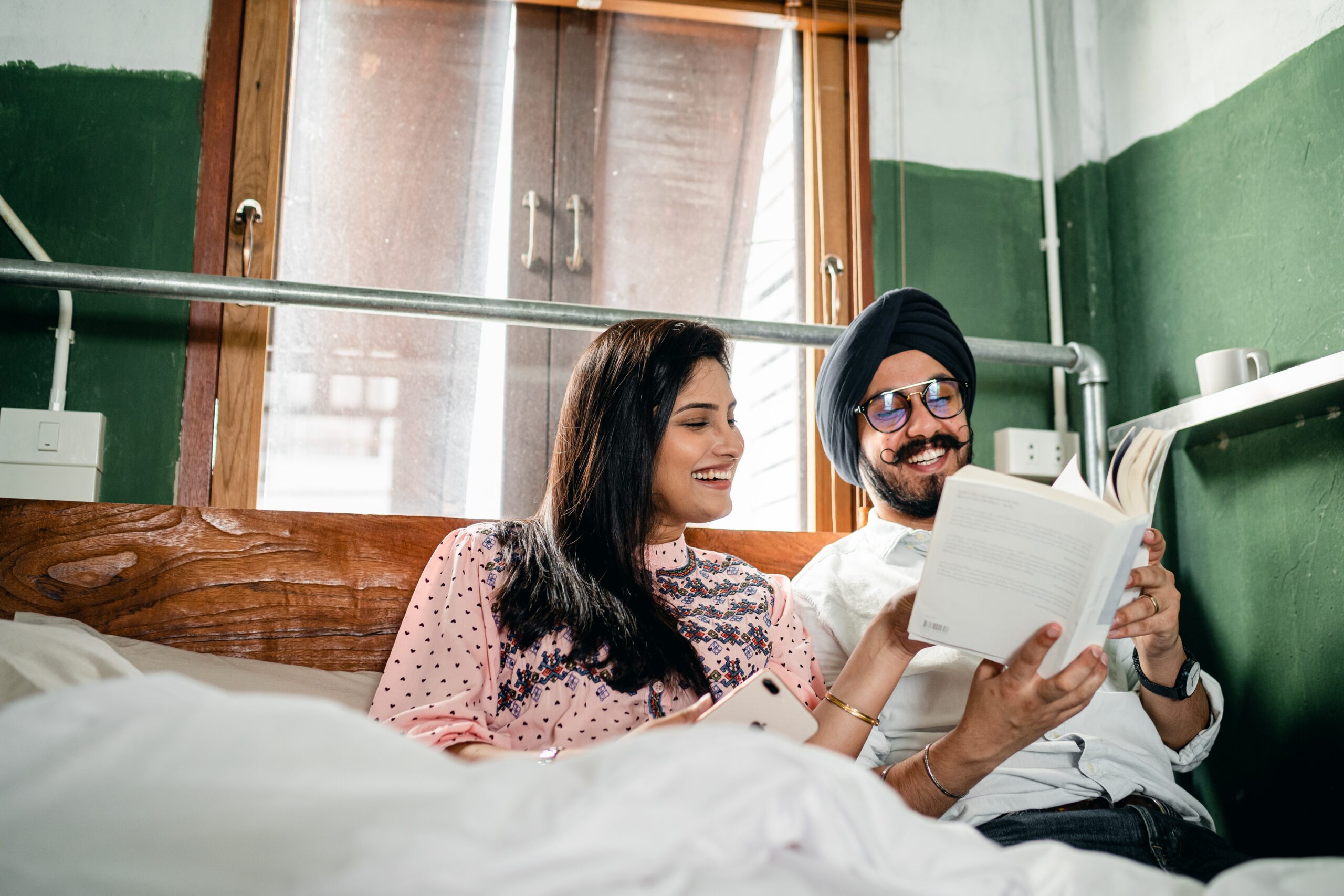 Una joven pareja de la india se sienta en la cama riendo juntos leyendo un libro