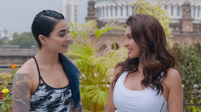 Samara and Umang talking to eachother while outside in a terrace. Both are smiling.