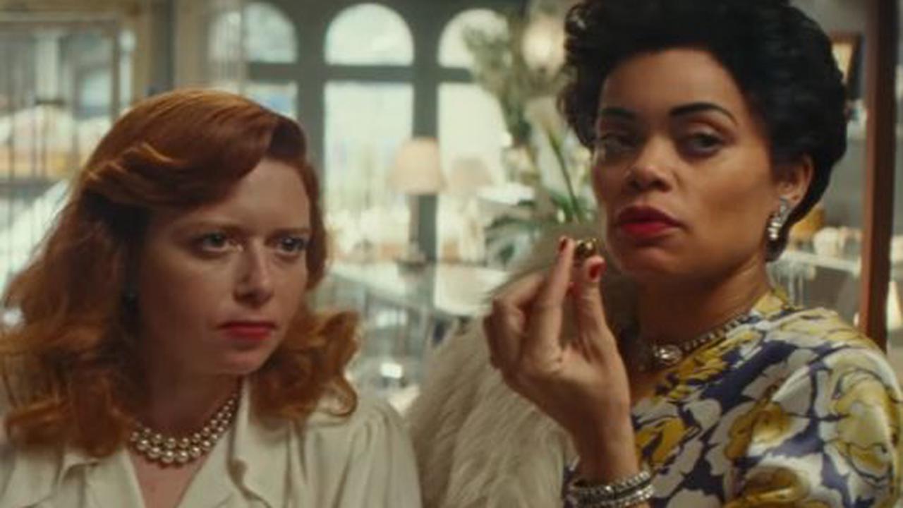 /Imagen de Lady Day y Tallulah Bankhead sentadas una al lado de la otra con una mirada molesta haciab alguien fuera de vista. Day tiene algo entre los dedos que sostiene.