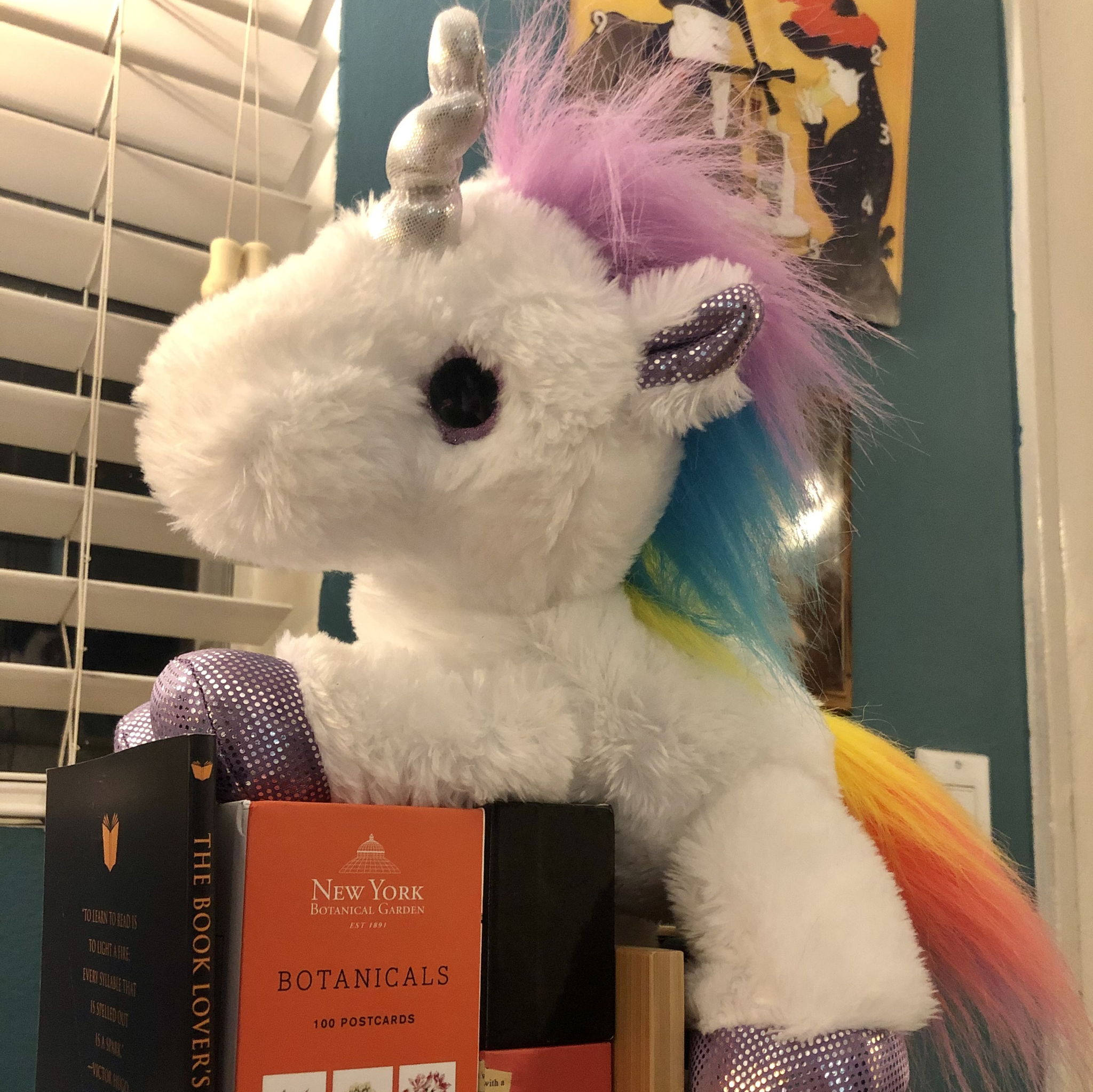 Un unicornio peluche con pelo de colores encima de unos libros.