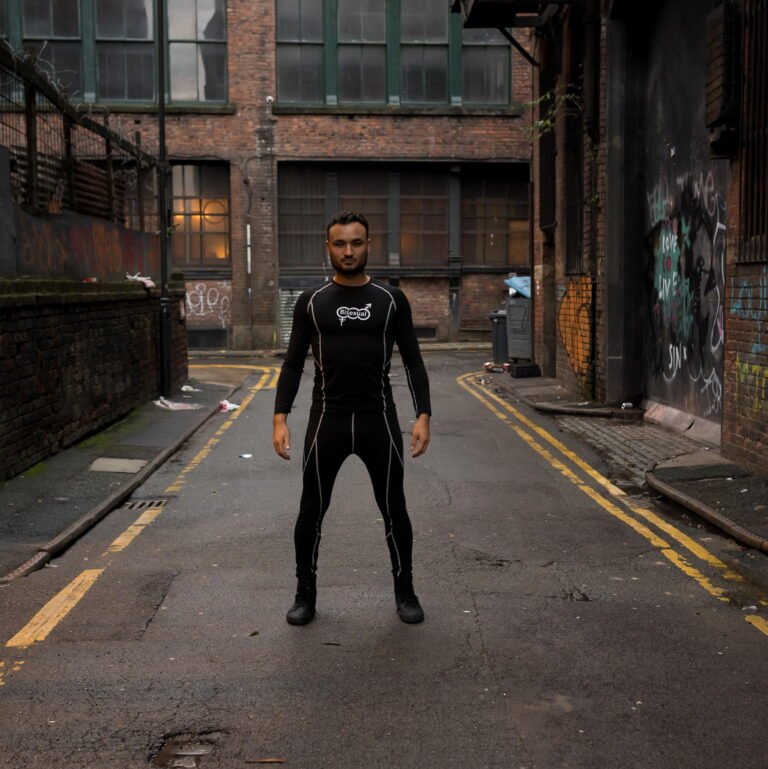 A model photograph of Lewis Oakley standing confidently in the middle of a street wearing dark clothing