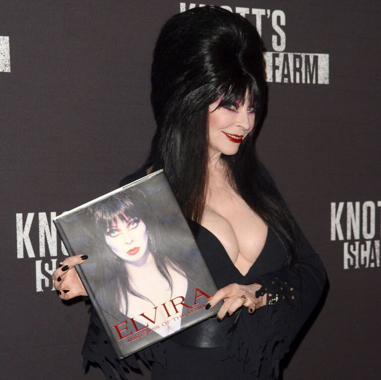 Elvira at the 2016 Knott's Scary Farm at Knott's Berry Farm  holding her book and smiling.