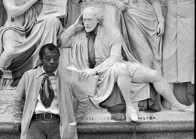 Black and white photo of Jams Baldwin posing with statue of Shakespeare.