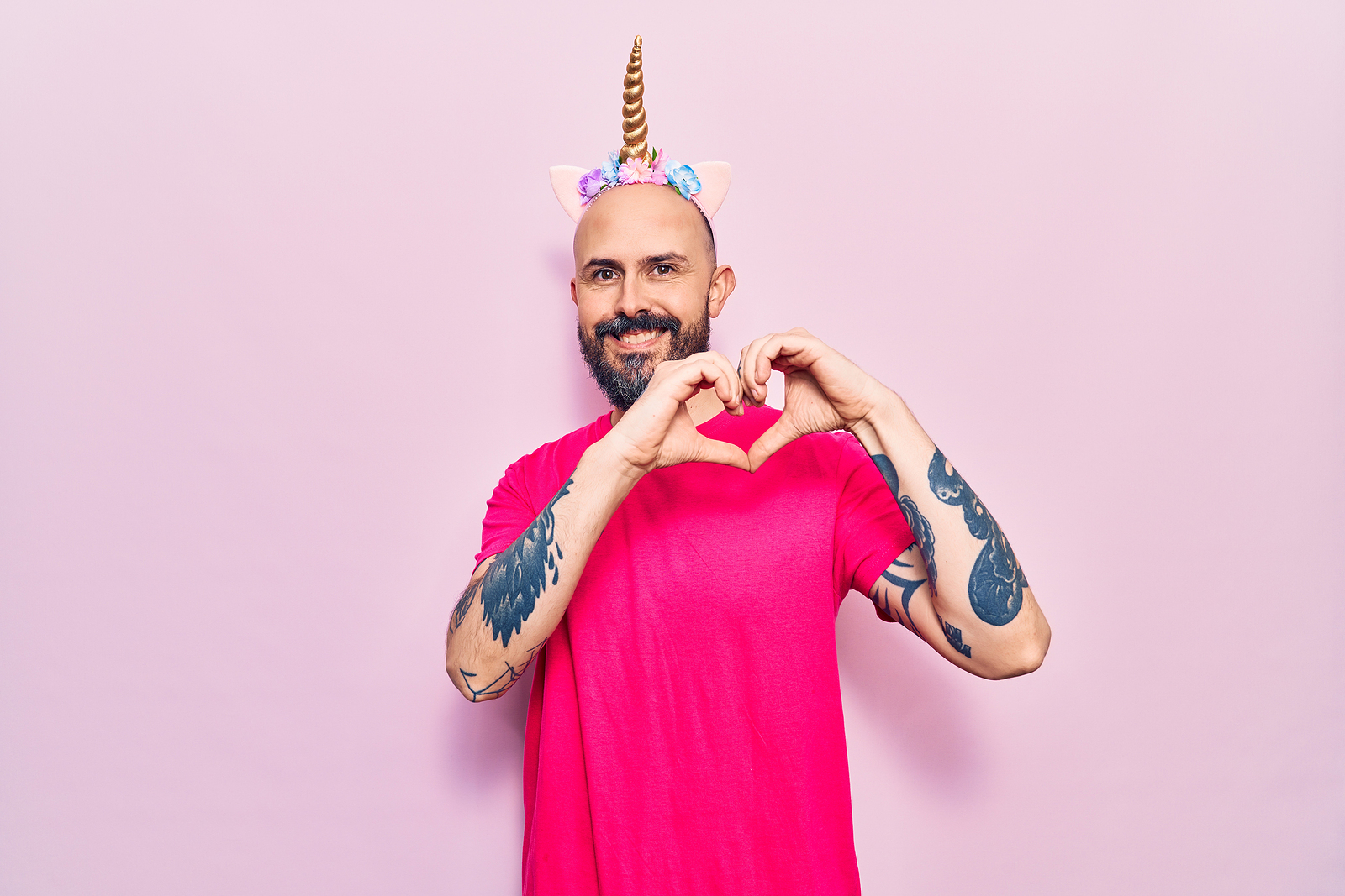 A young handsome man wearing unicorn diadem smiling doing heart symbol shape with hands