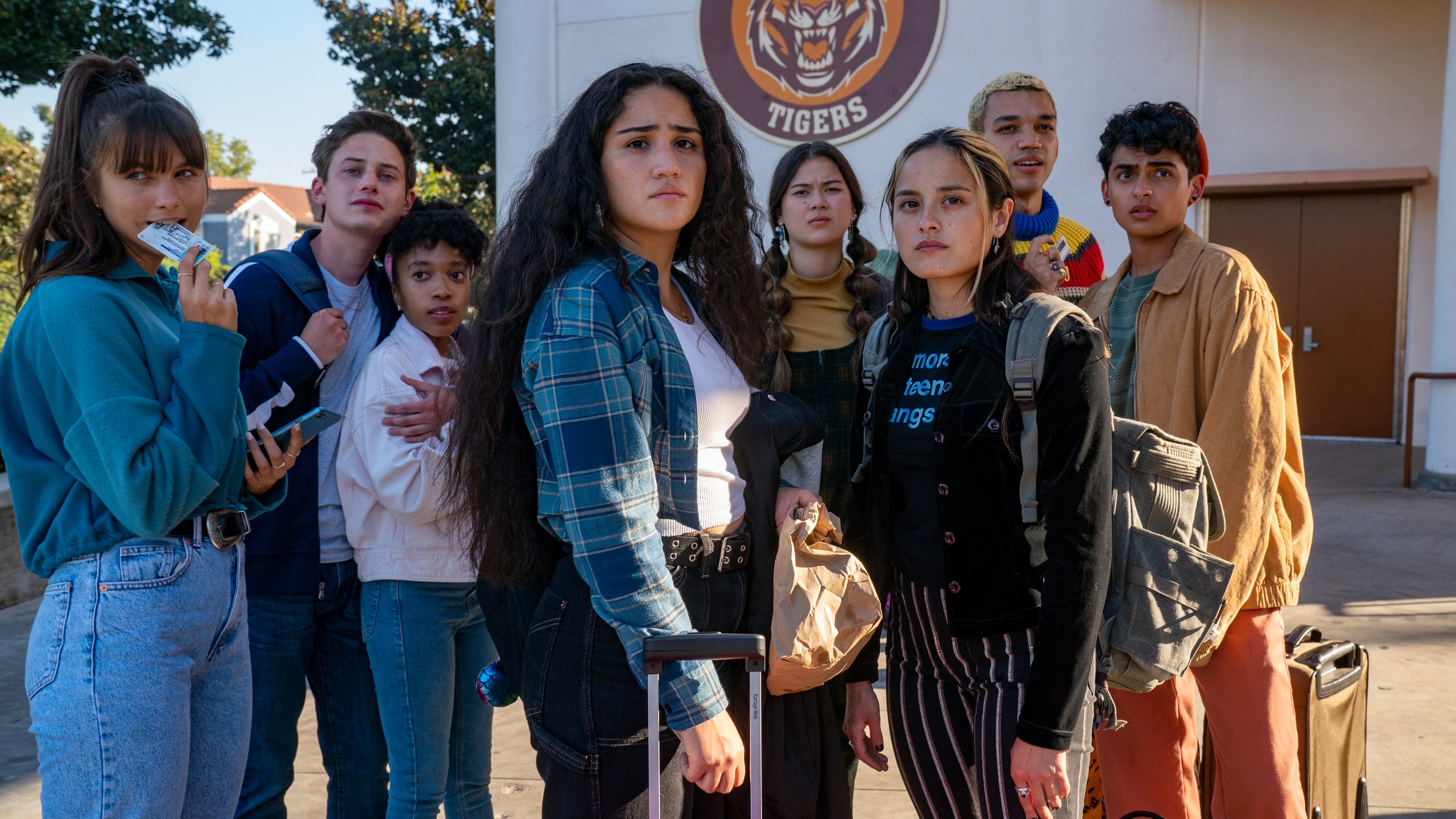 Cast of Generation and other classmates standing together looking at someone with serious expressions.