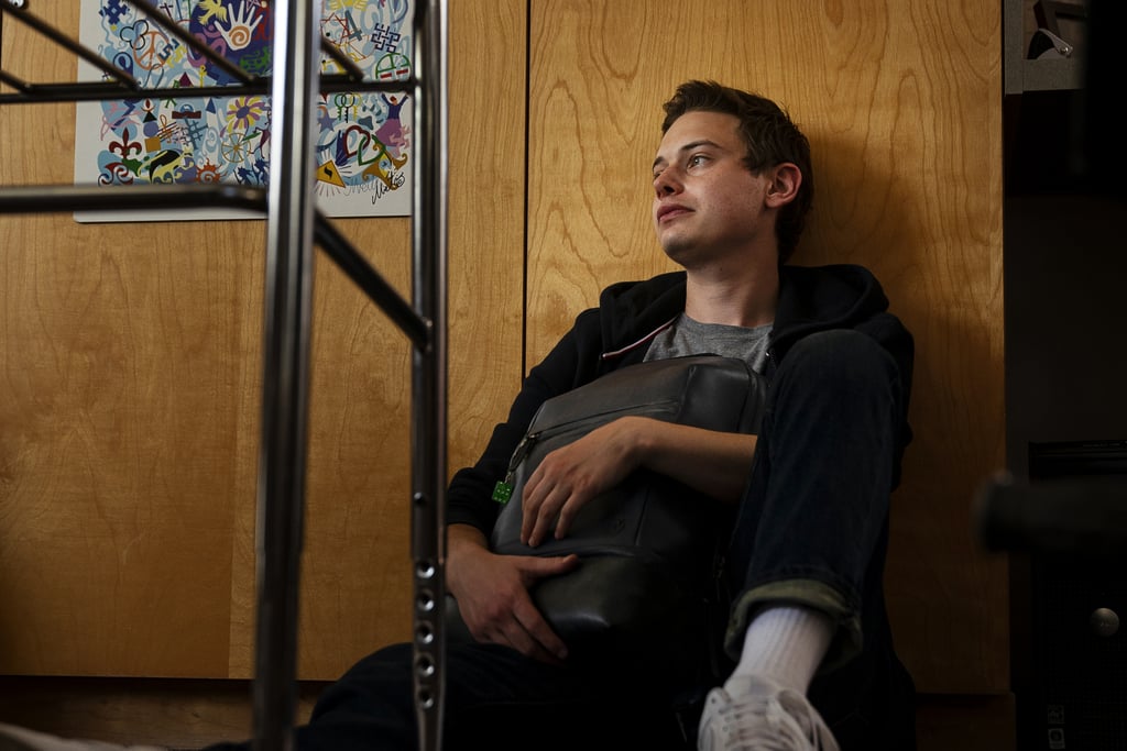 Nathan clutching his backpack sitting on the floor of a classroom looking at the window.