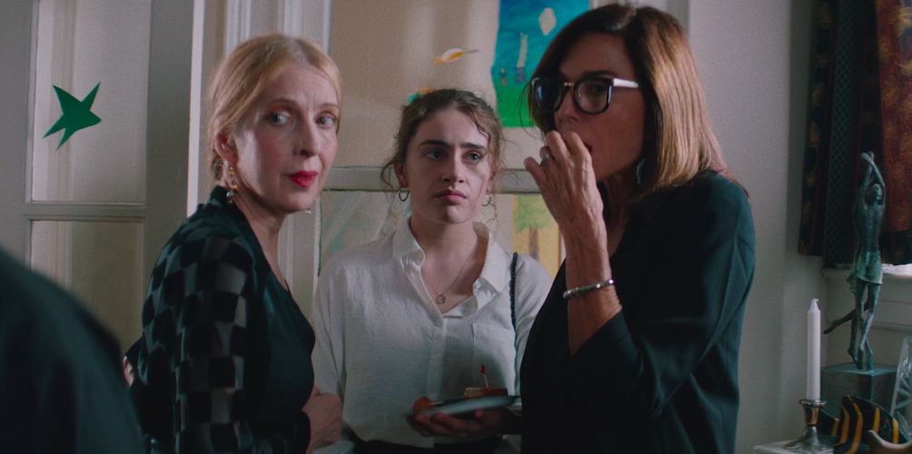 Danielle in between her mother and relative who are gossiping about someone off camera. Danielle looks at her mother with annoyance.