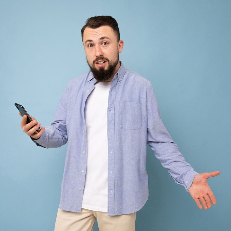 Surprised young man with a phone in his hands against a background of a blue wall