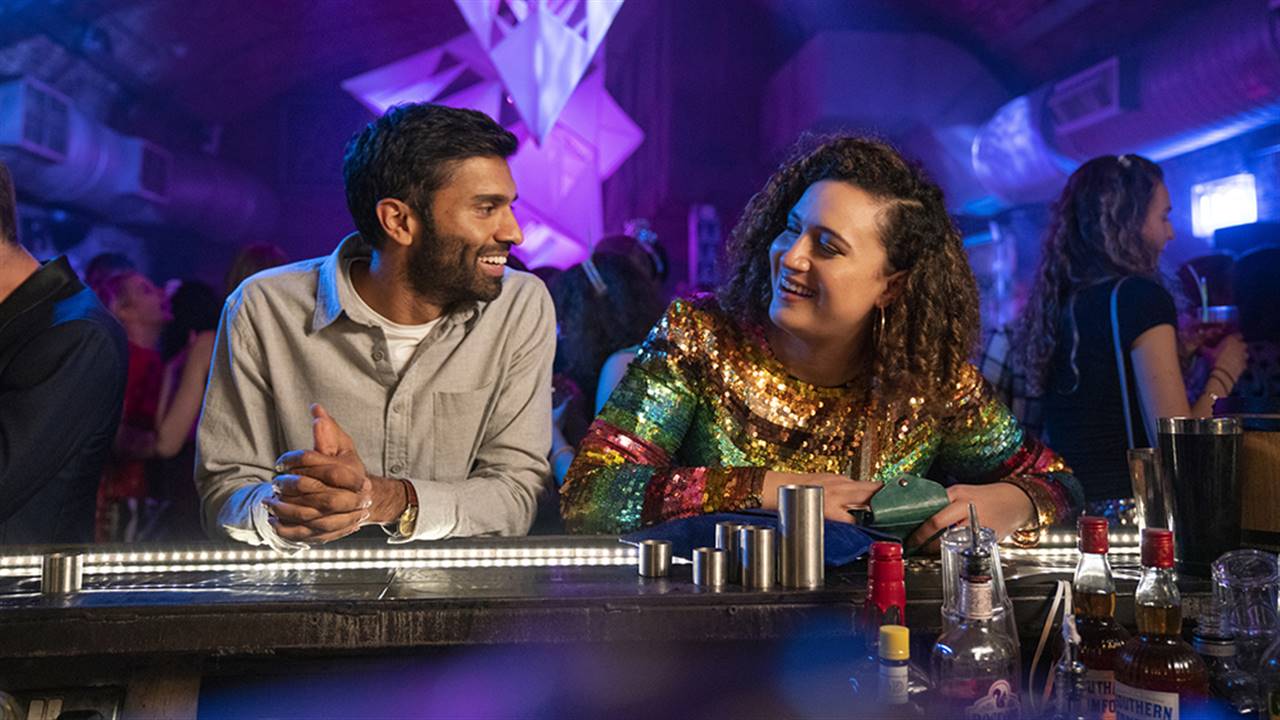 Jessie talking to Tom at the new years eve bar. Both are smiling.