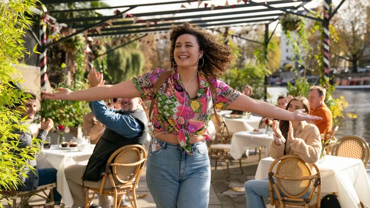 Jessie walking through an outdoor seating with arms stretched out walking confidently and smiling while others clap.