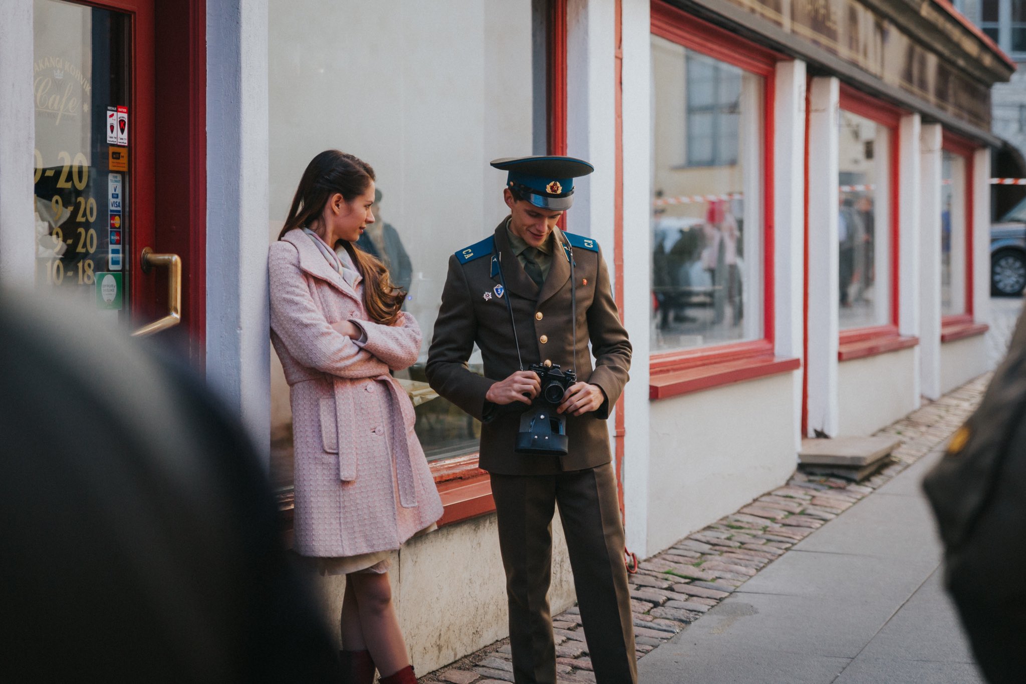 Sergei talking to Louis while wearing his unicorn. Both are against a shop.
