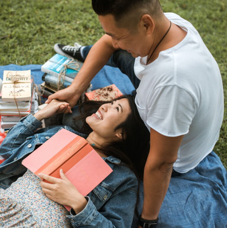 An Asian couple lay on the grass having a picnic together and laughing.