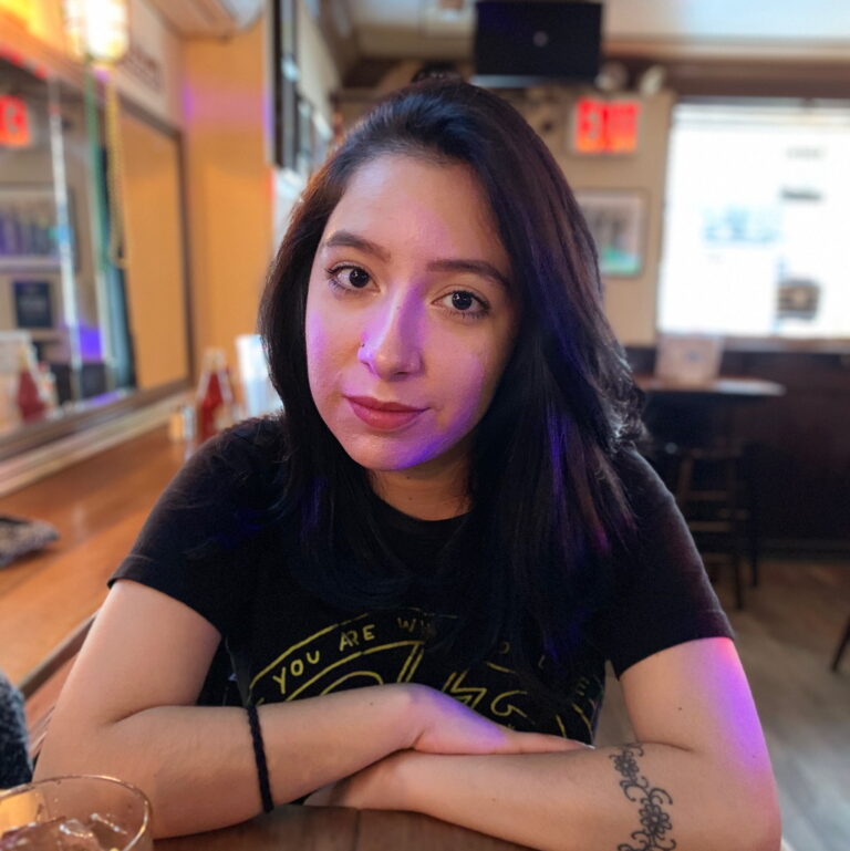 Andrea Mosqueda sitting at a cafe smiling with her arms folded.