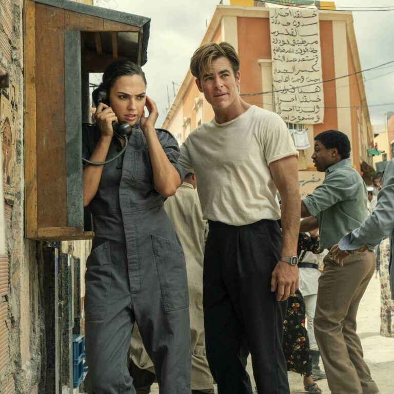 Wonder Woman and Steve looking cautiously around them while in a Middle Eastern country.Wonder Woman is on a public phone.