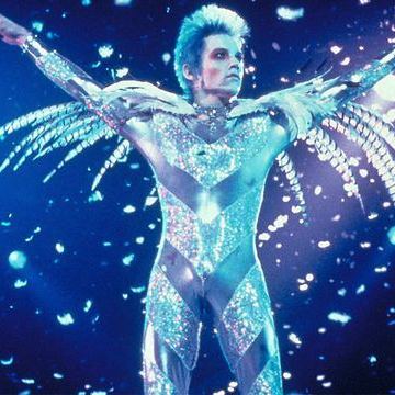 Brian as Tommy Stone wearing an elaborate silver and glitter costume with feathers performing onstage.