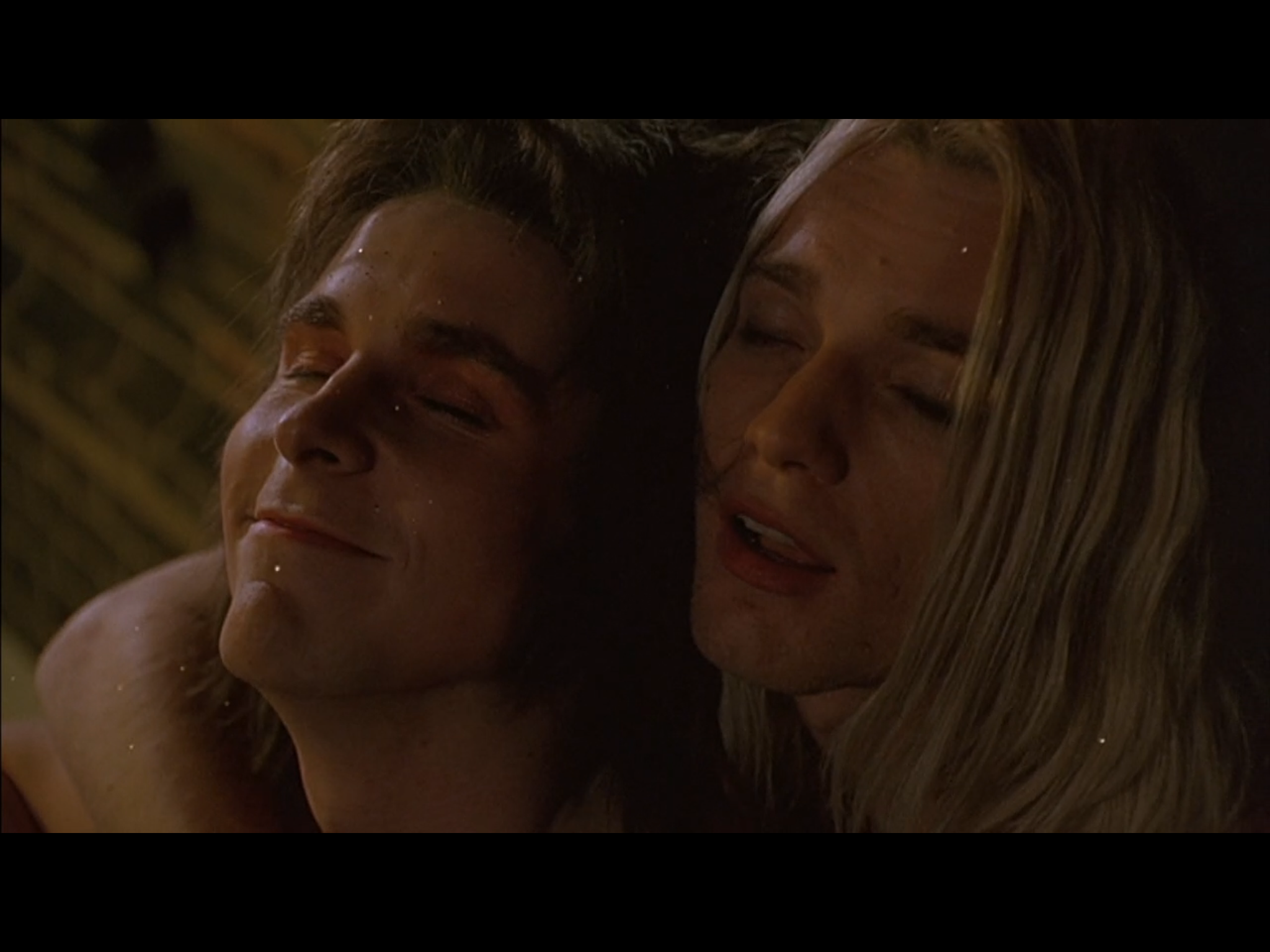 Brian holding Arthur in his arms as they both sit together. Both have their eyes closed and Arthur is smiling.