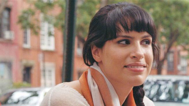 Shirin giving a half smile looking to the side while in the street.