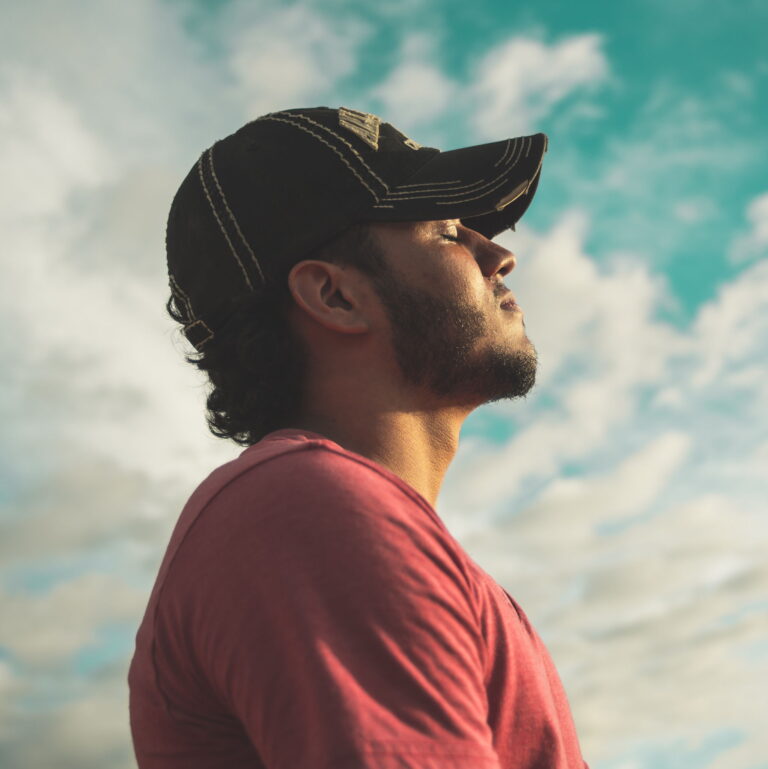 A man wearing a baseball cap looks out into the sky with his eyes closed and a smile.