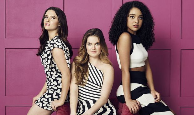 Jane, Sutton, and Kat posing in red and black dresses looking intently at the camera with a deep pink background.