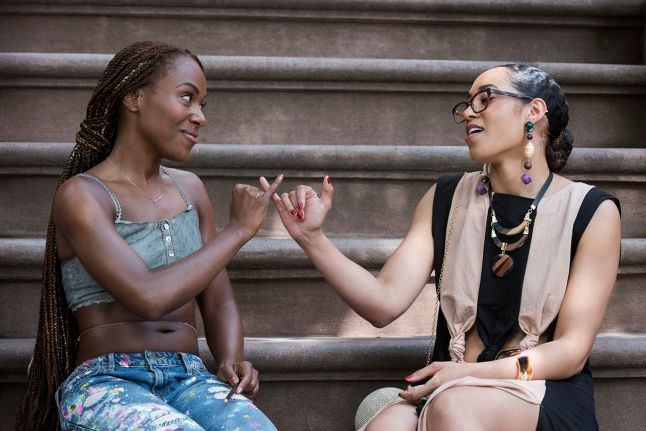 Nola y Opal sentadas juntas en los escalones de una casa cruzando sus dedos me&ntilde;iques sonriendo.
