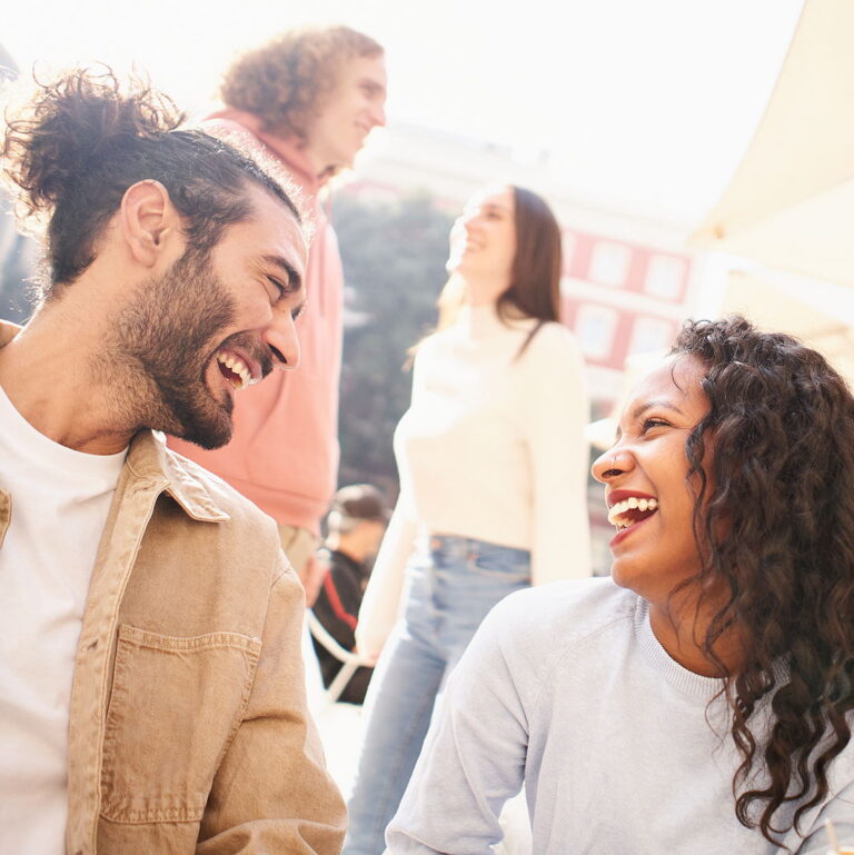 4 multi ethnic and attractive friends in athletic clothing locking arms and smiling for the camera with a basketball on someones lap.