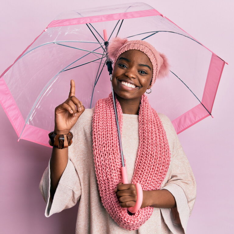 A black person wearing a beanie and yellow sweater, holding a large umbrella that is focused on the bi pride colors.