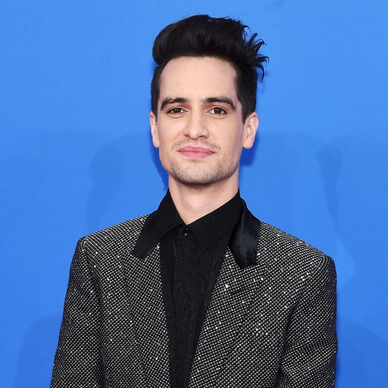 Brendon Urie at a carpet event wearing a balzer and smiling calmly.