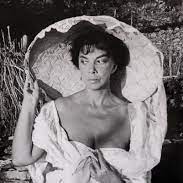 Black and white image of Leonor posing, holding a clear globe with her head inside it seeing through and smirking.