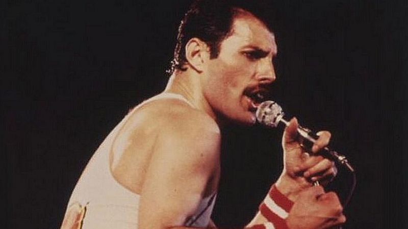 Una vieja imagen de Freddie con una camiseta blanca de tirantes cantando profundamente en el micr&oacute;fono.