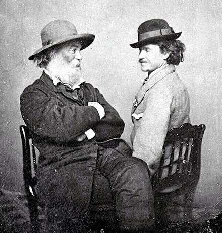 Wal Witman y Peter Doyle sentados sentados sobre unas sillas al estilo confidente, vestidos de traje y sombrero.