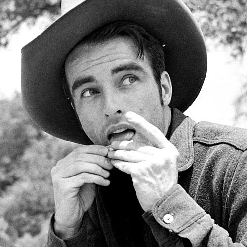 Black and white image of Montgomery Clift wearing a cowboy hate and preparing a cigarette.