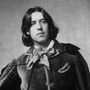 A black and white image of Oscar Wilde with hair up to his neck and a calm expression.