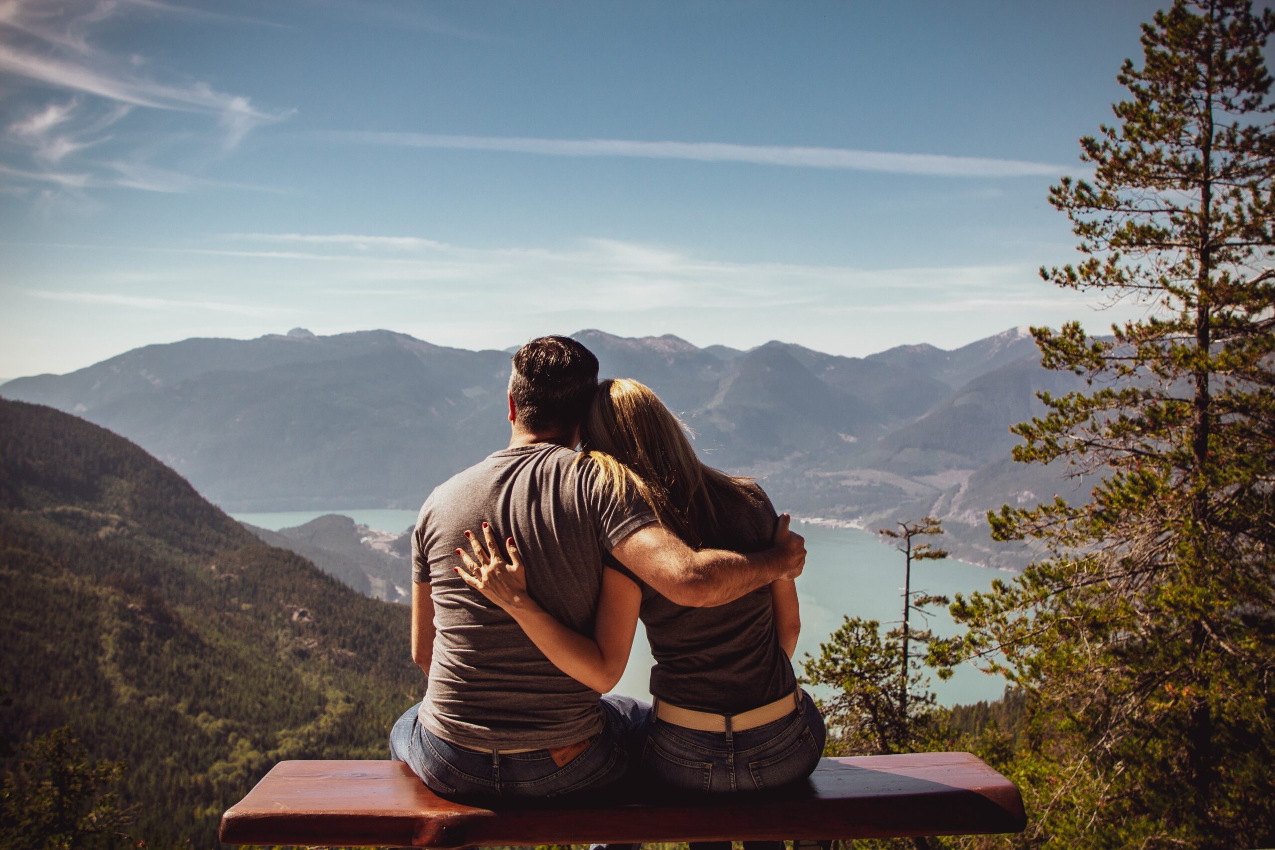 A man and a woman sit on a bench overlooking a beautiful scenery holding eachother.