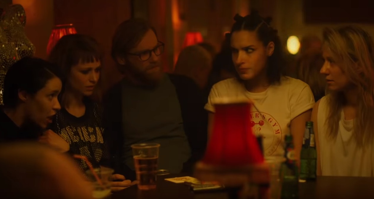 Friends of Leila sitting around a table at a bar with serious expressions on their faces.