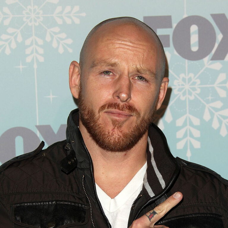 Jason Ellis at a carpet event looking at the camera making a gesture with both his hans.