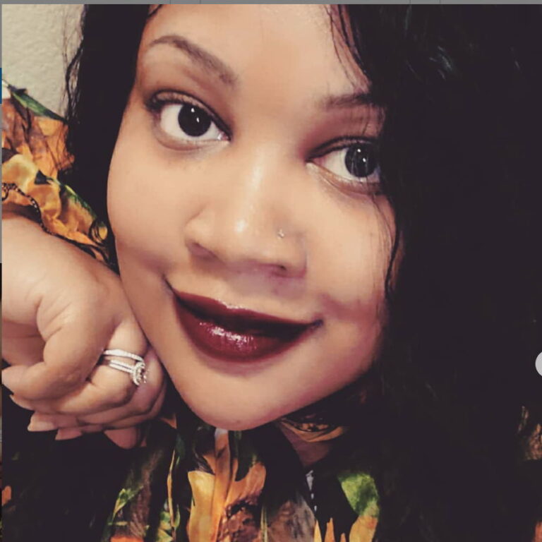 Tiffany smiling wearing a colorful blouse while her hand is to her chin.