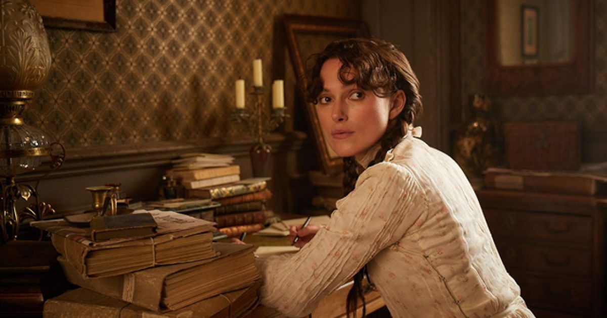 Colette writing something on a desk. She has her body turned to look at someone talking to her. /