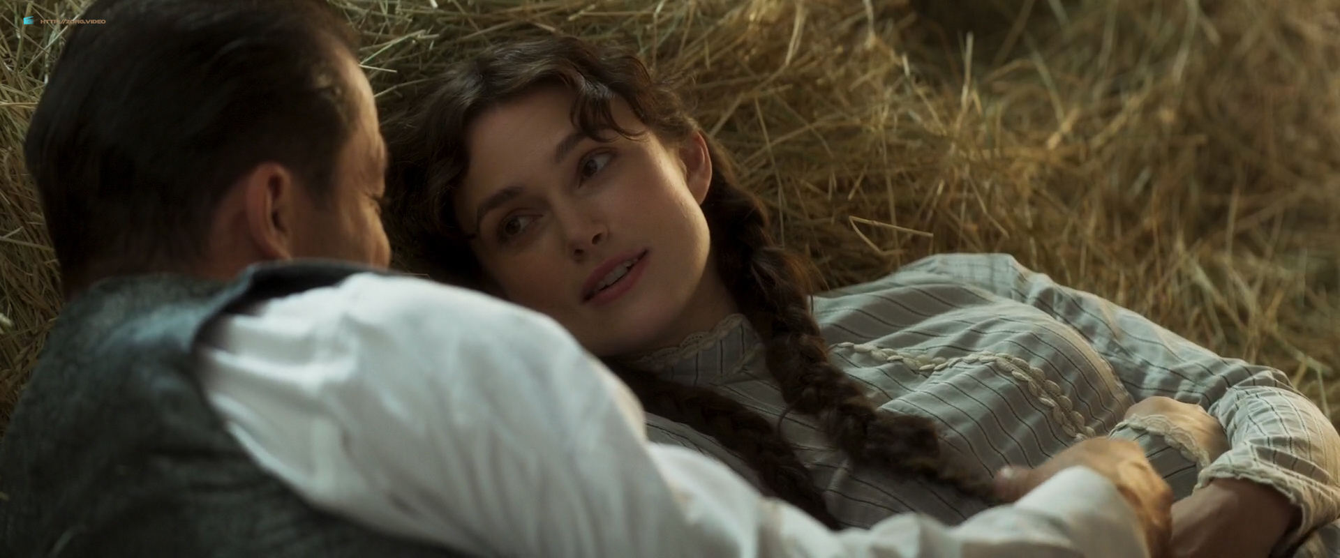 Collette and Willy laying on hay together, sharing an intimate conversation.