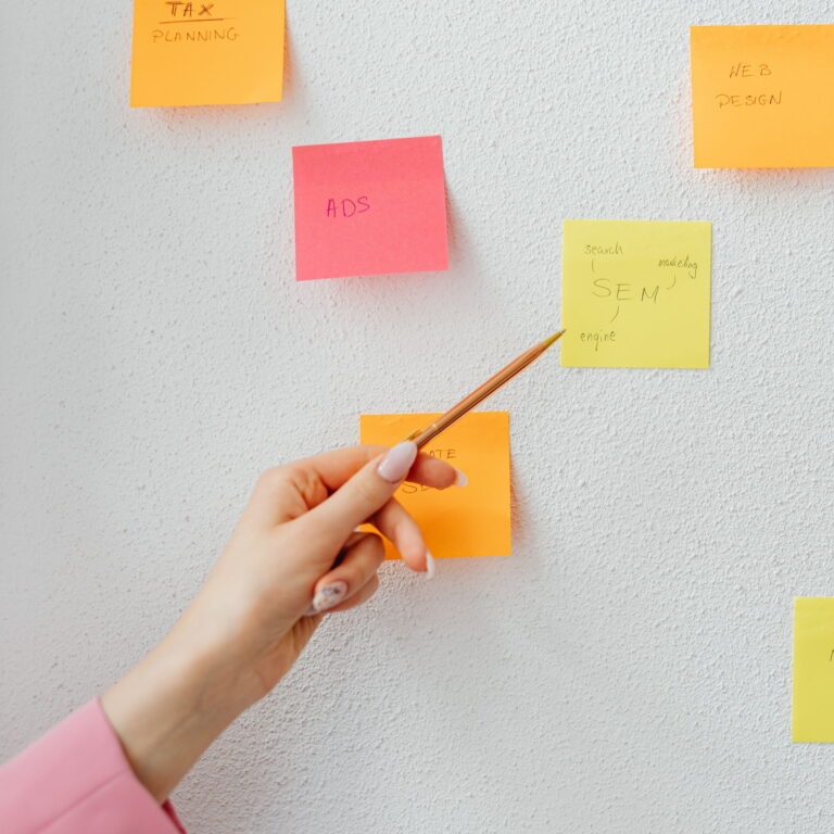 A hand pointing with a pencil to several colorful sticky notes.