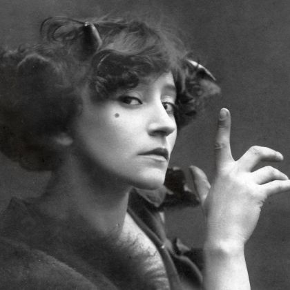 Colette looking to her side with her hand pointing up close to her face.