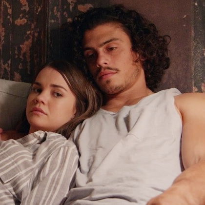 Callie leans on Gael. They are laying on a bed together both with mournful expressions.