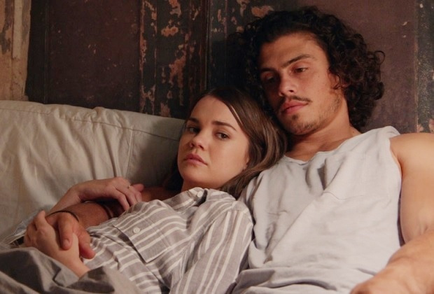 Callie leans on Gael. They are laying on a bed together both with mournful expressions.