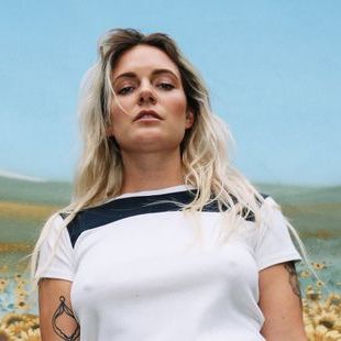 Tove Lo looking down towards the camera in front of a sunflower field.