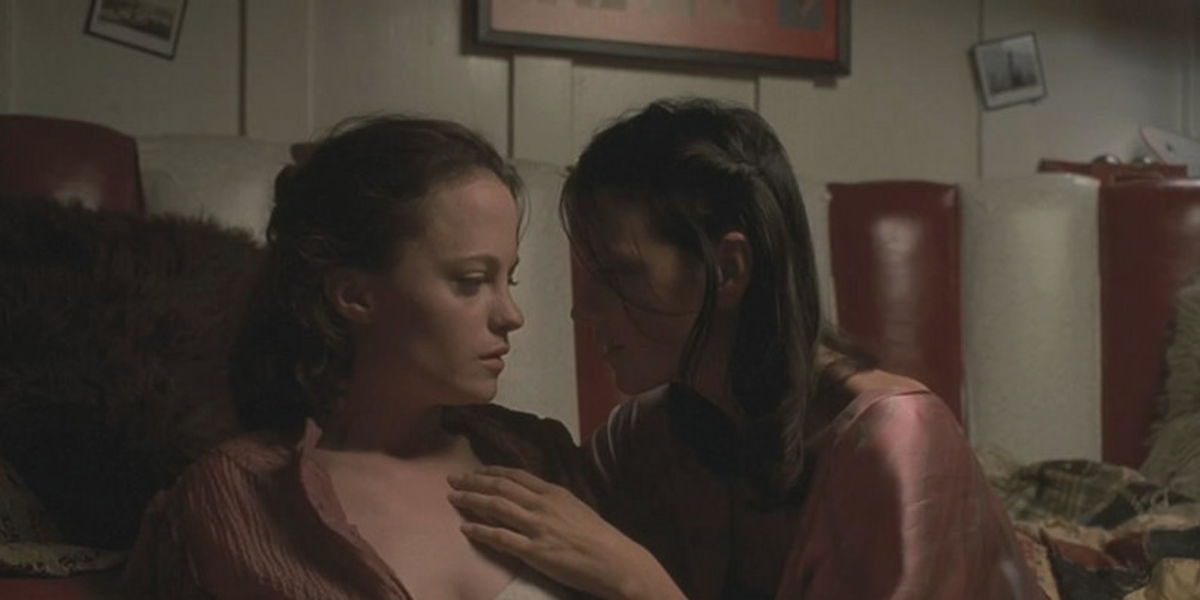 May and Polly sitting close together looking into eachothers eyes. Polly has her hand on May's neck.